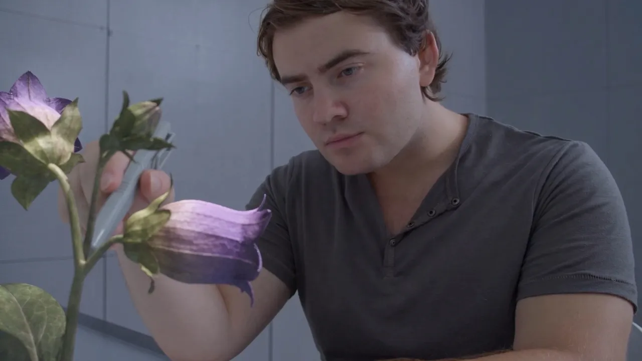 Luke LeBrun as Carter, studying purple flowers with a handheld device.