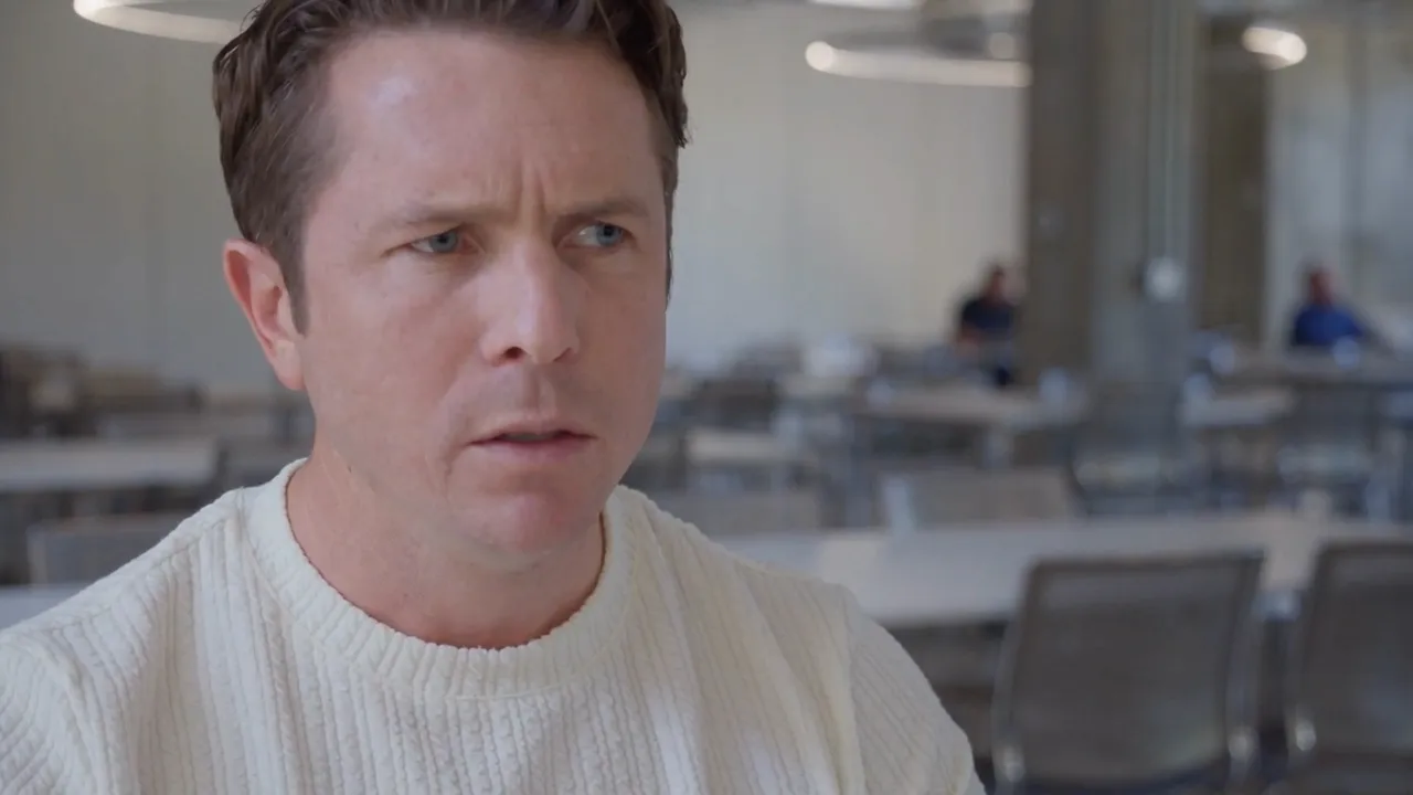 Eric Newcombe as Rick, looking concerned during a conversation in a café.