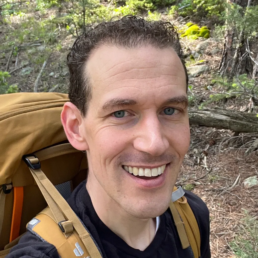 Ryan smiling on a forest hiking trail, wearing a backpack.