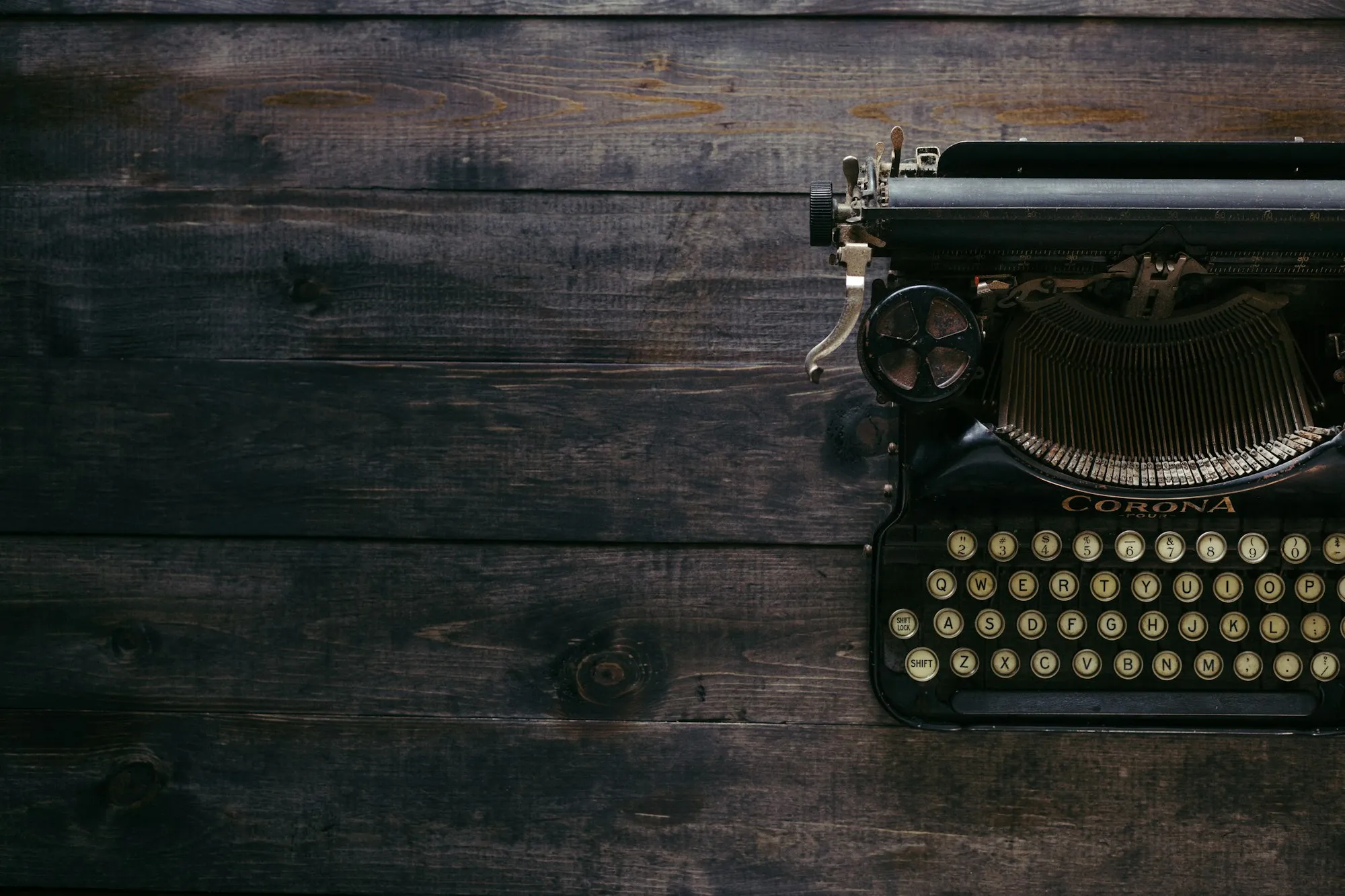 An antique Corona typewriter resting on dark weathered wooden planks.